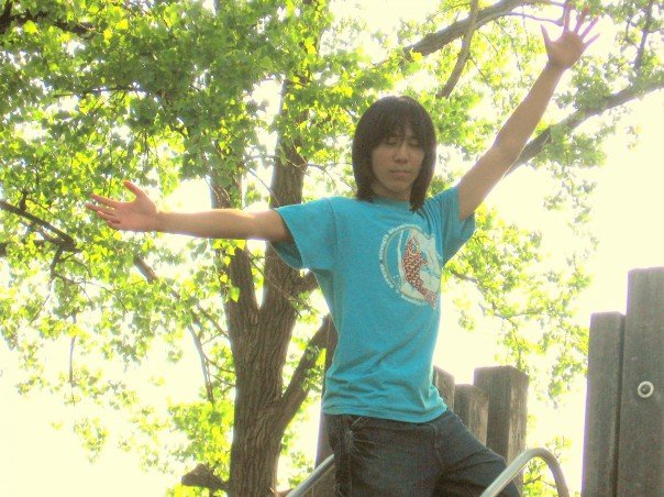 Marina standing on playground equipment with her eyes closed and arms spread wide. Trees in the background are lit brightly and majestically.