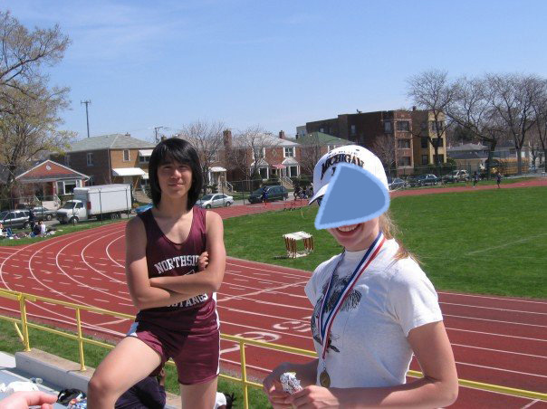 Marina in her track uniform, standing on bleachers in front of a track.