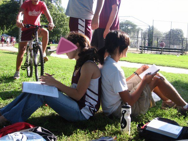 Marina sitting in the grass, back to back with a friend, at a cross country meet.