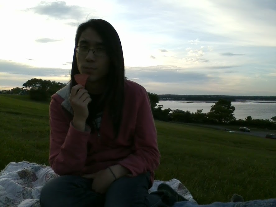 Marina sitting on a grassy hill, eating a chip in the waning light.