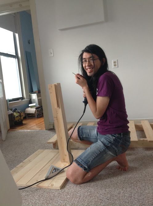 Marina stands next to a partly assembled bed with a drill.