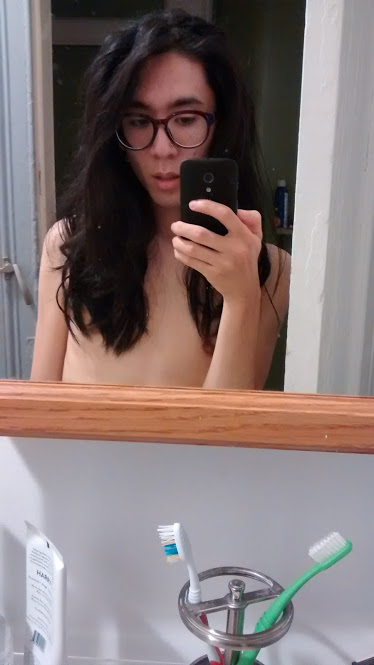A topless bathroom mirror selfie, highlighting the dramatic wavy hair Marina got for the costume.