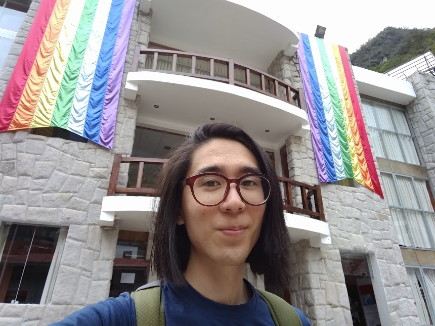 Marina standing in front of the Cusco flag, which has rainbow stripes.